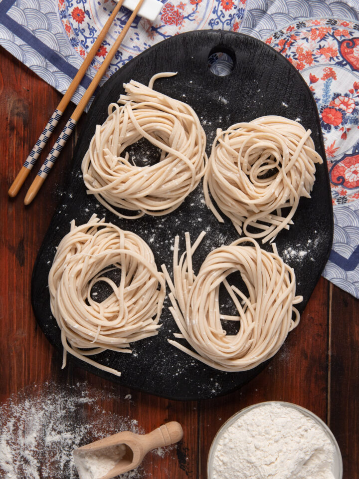 Noodles disposti in 4 nidi su piatto nero, con tovaglietta orientale e bacchette cinesi