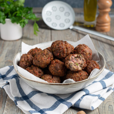 piatto da portata con polpette di carne fritte, schiumarola sullo sfondo, olio e pepe