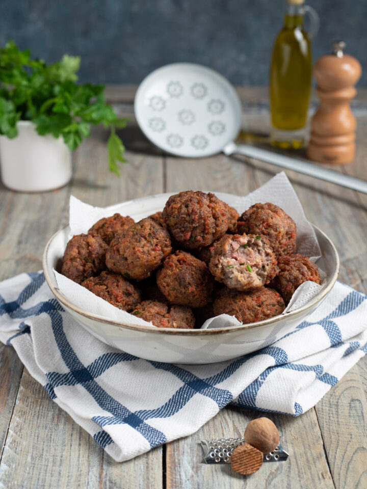 piatto da portata con polpette di carne fritte, schiumarola sullo sfondo, olio e pepe