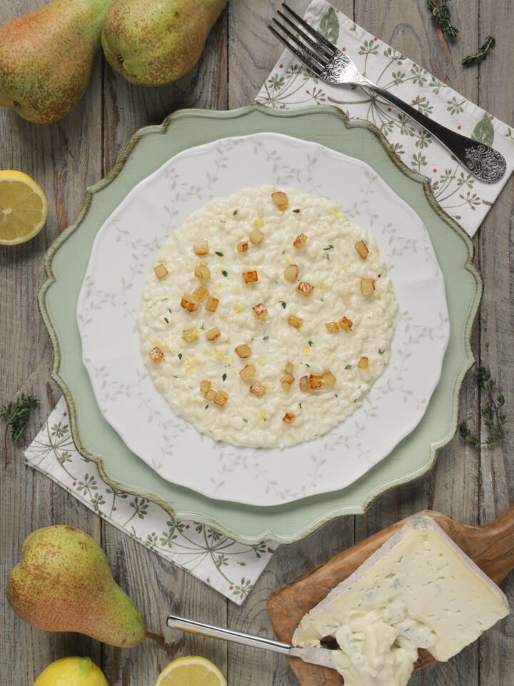 Risotto gorgonzola e pere su piatto bianco e sottopiatto verde decorato con fetta di formaggio intera