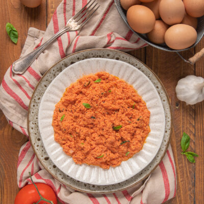 Uova strapazzate al pomodoro su canovaccio bianco a righe rosse, cestino di uova, pomodoro, aglio e foglioline di basilico