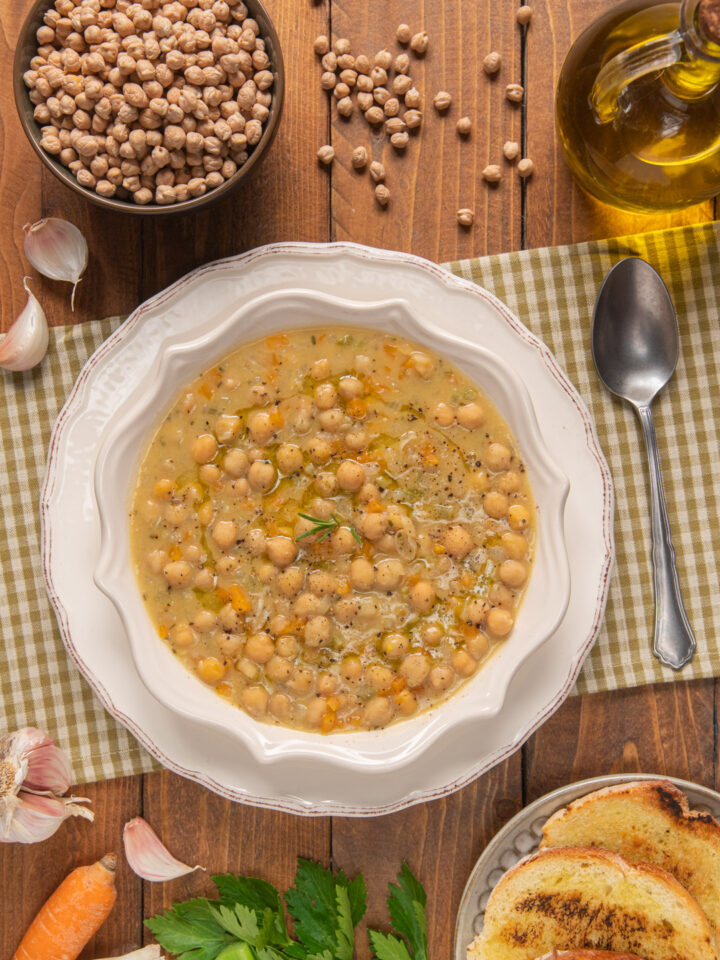 Zuppa di ceci su t tovaglietta a quadretti, ceci secchi, carota, basilico, ampolla d'olio e fette di pane abbrustolito