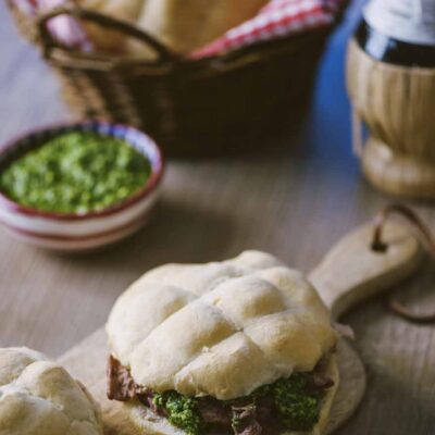 panino col lampredotto su tagliere di legno, ciotola con salsa verde e cestino con pane