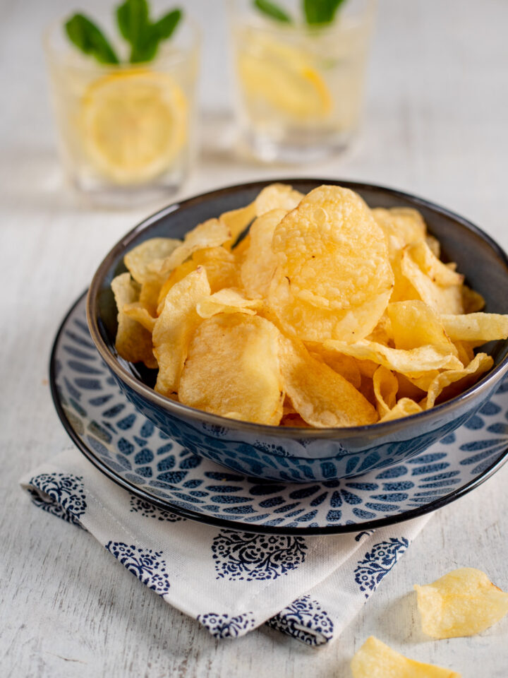 ciotolina con chips di patate e drink sullo sfondo