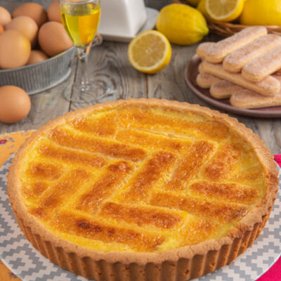 Crostata beneventana intera, con decoro a lisca di pesce, savoiardi sullo sfondo, uova e limone tagliato a metà