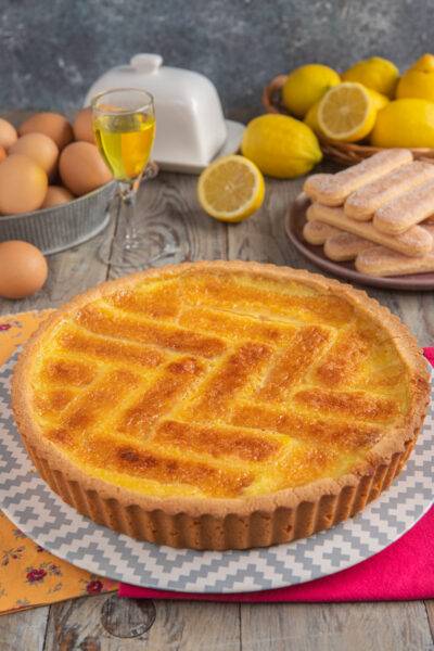 Crostata beneventana intera, con decoro a lisca di pesce, savoiardi sullo sfondo, uova e limone tagliato a metà