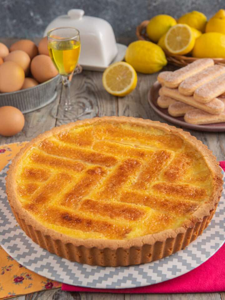 Crostata beneventana intera, con decoro a lisca di pesce, savoiardi sullo sfondo, uova e limone tagliato a metà