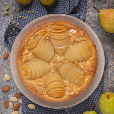 Torta Bourdaloue impiattata con attorno pere intere e mandorle pelate e non