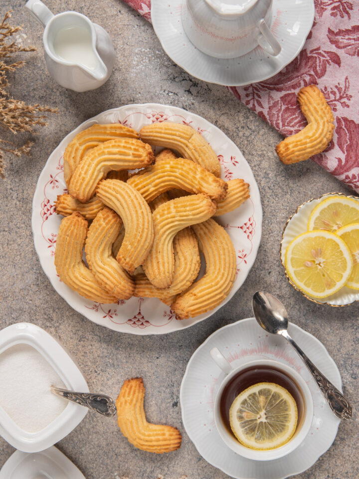 Krumiri su piatto tondo bianco decorato di rosso, con tazza di tè al limone, zucchero e fette di limone tagliate