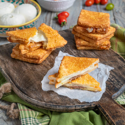 tagliere di legno con mozzarella in carrozza tagliata a metà, mozzarella fresca e acciughe