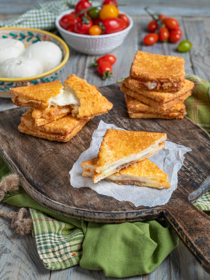 tagliere di legno con mozzarella in carrozza tagliata a metà, mozzarella fresca e acciughe