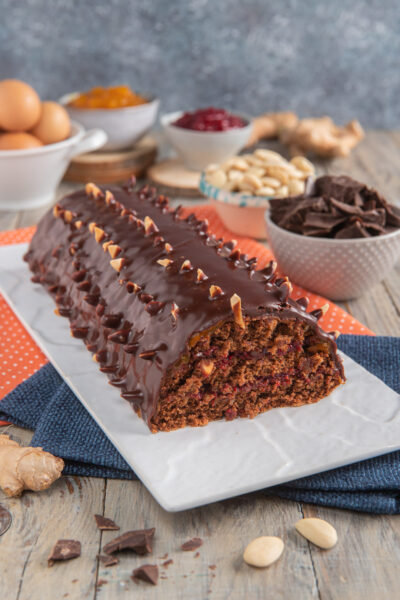 Torta al cioccolato con mandorle su piatto rettangolare bianco con ciotoline con pezzi di cioccolato, mandorle, confetture e uova intere