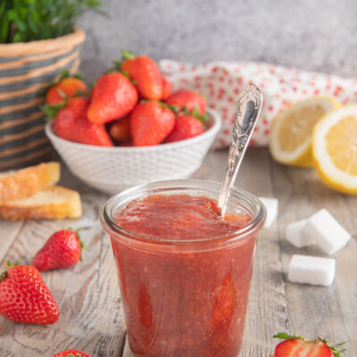 vasetto di vetro con confettura di fragole, fragole fresche e limoni sullo sfondo