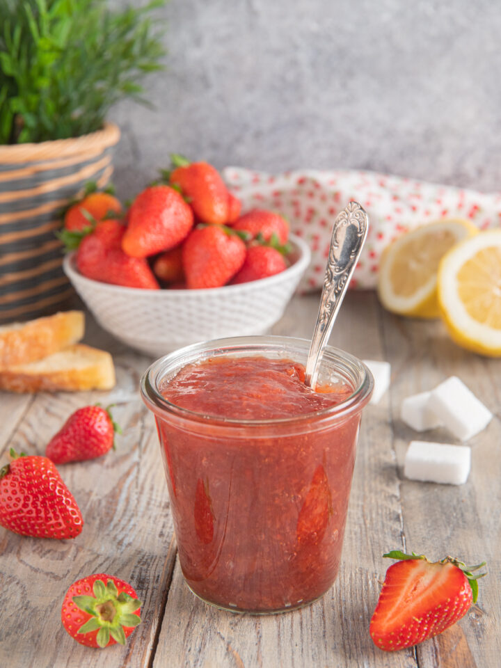 vasetto di vetro con confettura di fragole, fragole fresche e limoni sullo sfondo