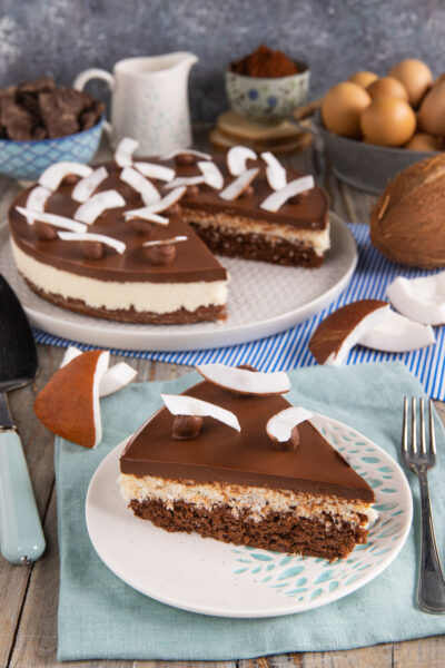 Una torta a strati composta da una base di soffice pasta biscotto al cacao, un inserto di crema di cocco e una golosa copertura al cioccolato