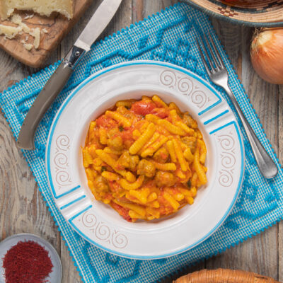 Un primo piatto di pasta fresca di semola a forma di conchiglietta, tipica della cucina sarda, con un condimento a base di salsiccia, pomodori, zafferano e pecorino sardo grattugiato