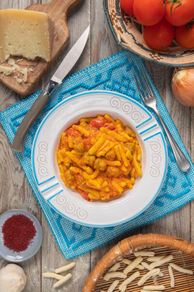 Un primo piatto di pasta fresca di semola a forma di conchiglietta, tipica della cucina sarda, con un condimento a base di salsiccia, pomodori, zafferano e pecorino sardo grattugiato