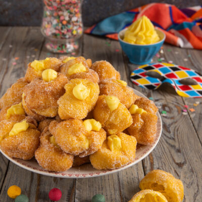 Le frittelle di Carnevale sono dolci fritti dorati e morbidissimi, ripieni di crema pasticcera e ricoperti di zucchero