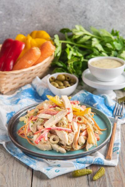 Un'insalata fresca e colorata, a base di pollo, peperoni, carote, olive, cetriolini sottaceto e fontina