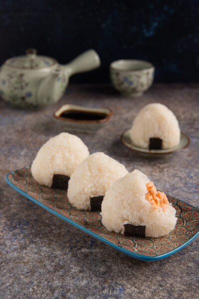 Gli onigiri sono una tipologia di sushi costituita da polpette di riso a forma triangolare con un ripieno di salmone e parzialmente avvolte da una striscia di alga Nori che le rende facili da mangiare con le mani