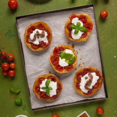 Le mini tatin ai pomodorini sono la rivisitazione salata e monoporzione di un celebre dolce francese apprezzato in tutto il mondo. Gli ingredienti? Pomodorini, miele, aceto balsamico, burrata, acciughe, pesto, capperi ed erbe aromatiche