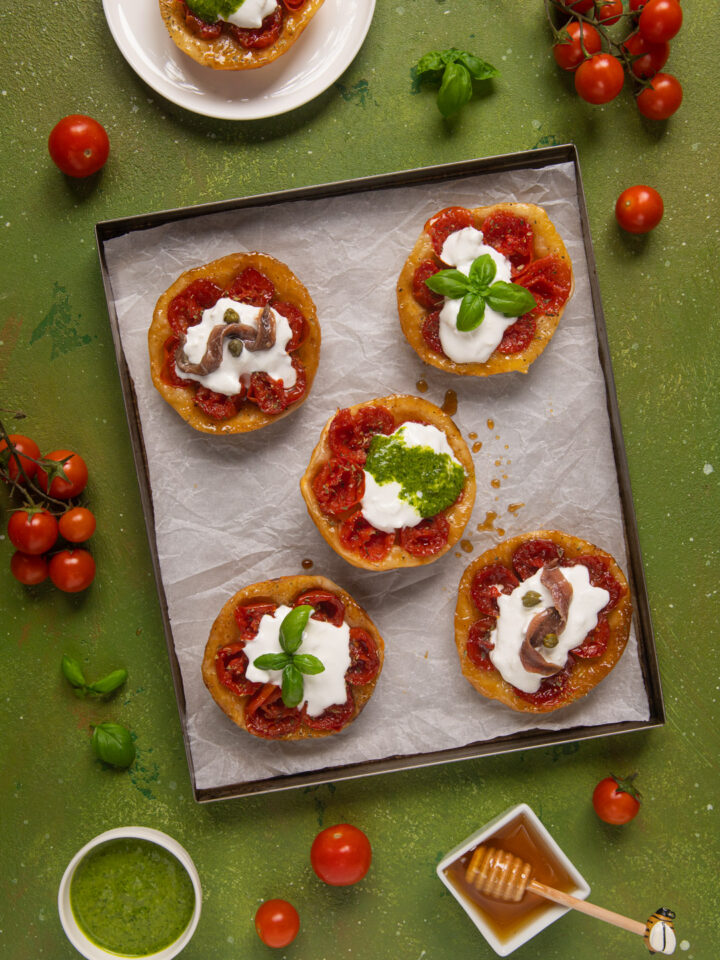 Le mini tatin ai pomodorini sono la rivisitazione salata e monoporzione di un celebre dolce francese apprezzato in tutto il mondo. Gli ingredienti? Pomodorini, miele, aceto balsamico, burrata, acciughe, pesto, capperi ed erbe aromatiche