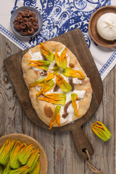 Un lievitato tipico della cucina laziale, che assomiglia un po' a una pizza, un po' a una focaccia, farcito in superficie con alici, fiori di zucca e burrata