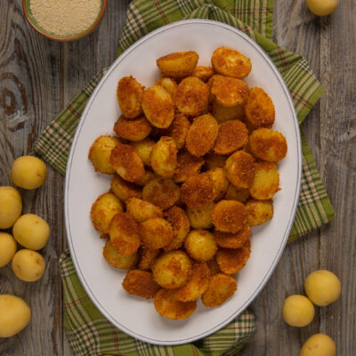 Una ricetta originale per servire le patate in modo diverso dal solito: cosparse di formaggio grattugiato, paprika, pangrattato e aglio in polvere e cotte al forno
