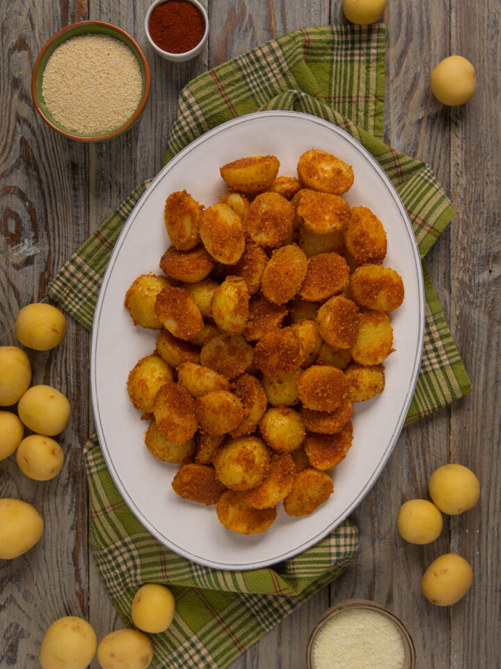 Una ricetta originale per servire le patate in modo diverso dal solito: cosparse di formaggio grattugiato, paprika, pangrattato e aglio in polvere e cotte al forno