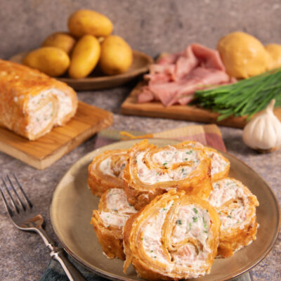 Rotolo di patate croccante con patate sottili e dorate al forno, avvolge un morbido ripieno di formaggi e prosciutto cotto.