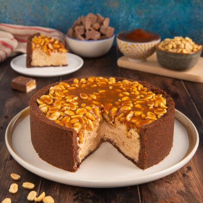 La torta Snickers, ispirata a un celebre snack è una sorta di cheesecake a base di biscotti, crema al formaggio, cioccolato e burro di arachidi con caramello salato