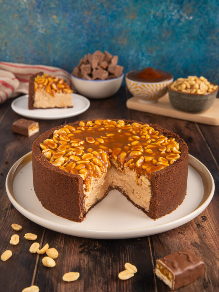 La torta Snickers, ispirata a un celebre snack è una sorta di cheesecake a base di biscotti, crema al formaggio, cioccolato e burro di arachidi con caramello salato