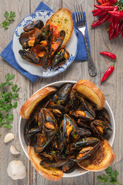 Le cozze alla tarantina sono un delizioso antipasto pugliese, in cui questo saporito mollusco viene condito con una salsa al pomodoro piccante, in cui intingere il rustico pane di Altamura
