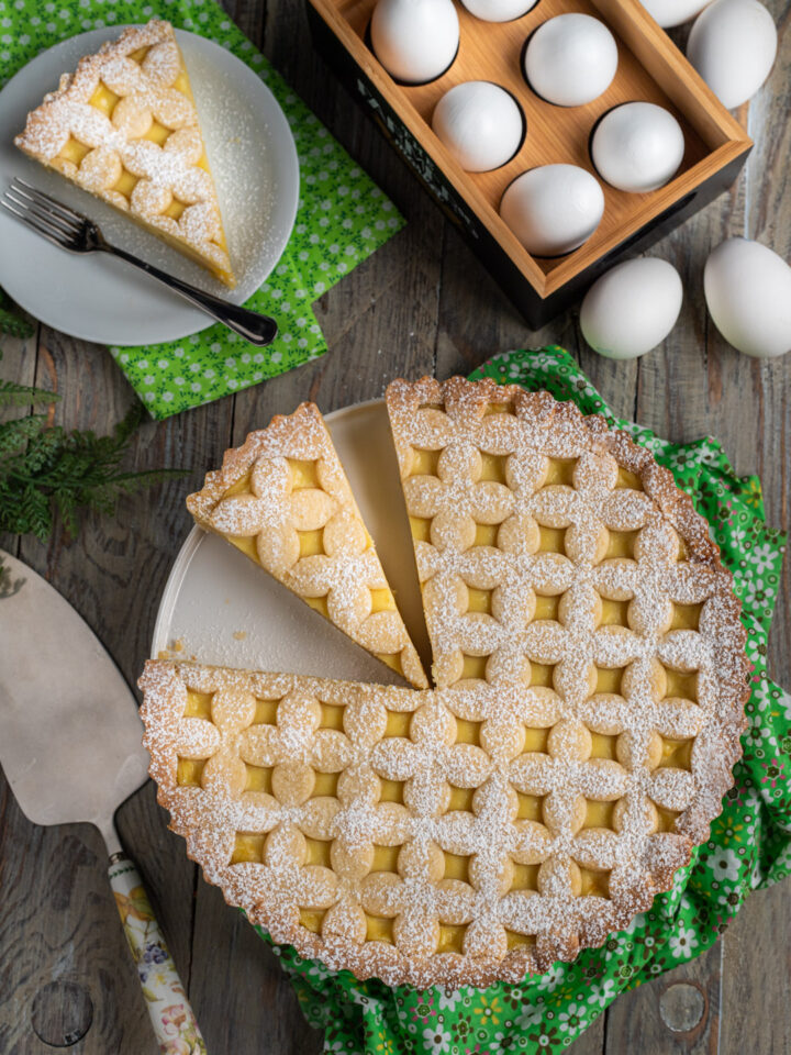 La crostata con la crema pasticcera è un dolce semplicissimo da preparare, con una base di pasta frolla, una farcitura vellutata profumata alla vaniglia e limone e una bella decorazione in superficie