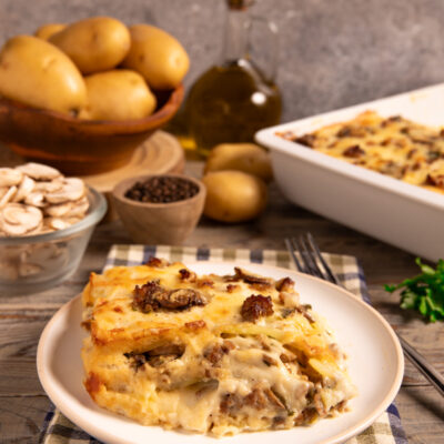 Parmigiana di patate funghi e salsiccia Una ricetta rustica, golosa e invernale, in bianco, con strati di besciamella e formaggi filanti.