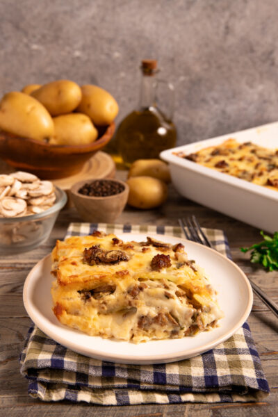 Parmigiana di patate funghi e salsiccia Una ricetta rustica, golosa e invernale, in bianco, con strati di besciamella e formaggi filanti.