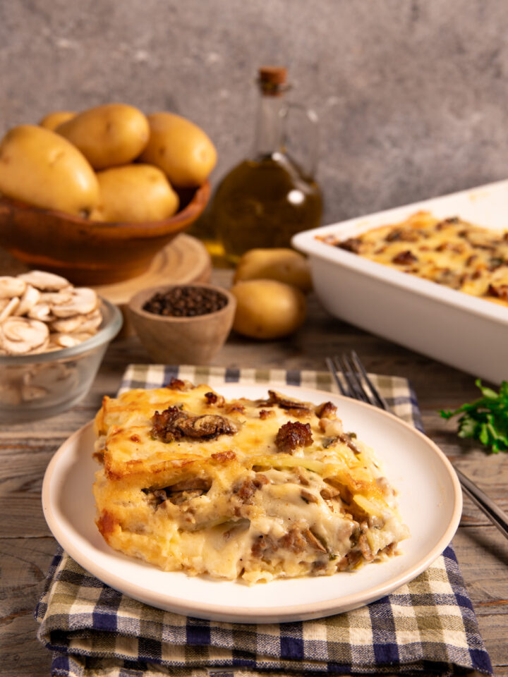 Parmigiana di patate funghi e salsiccia Una ricetta rustica, golosa e invernale, in bianco, con strati di besciamella e formaggi filanti.